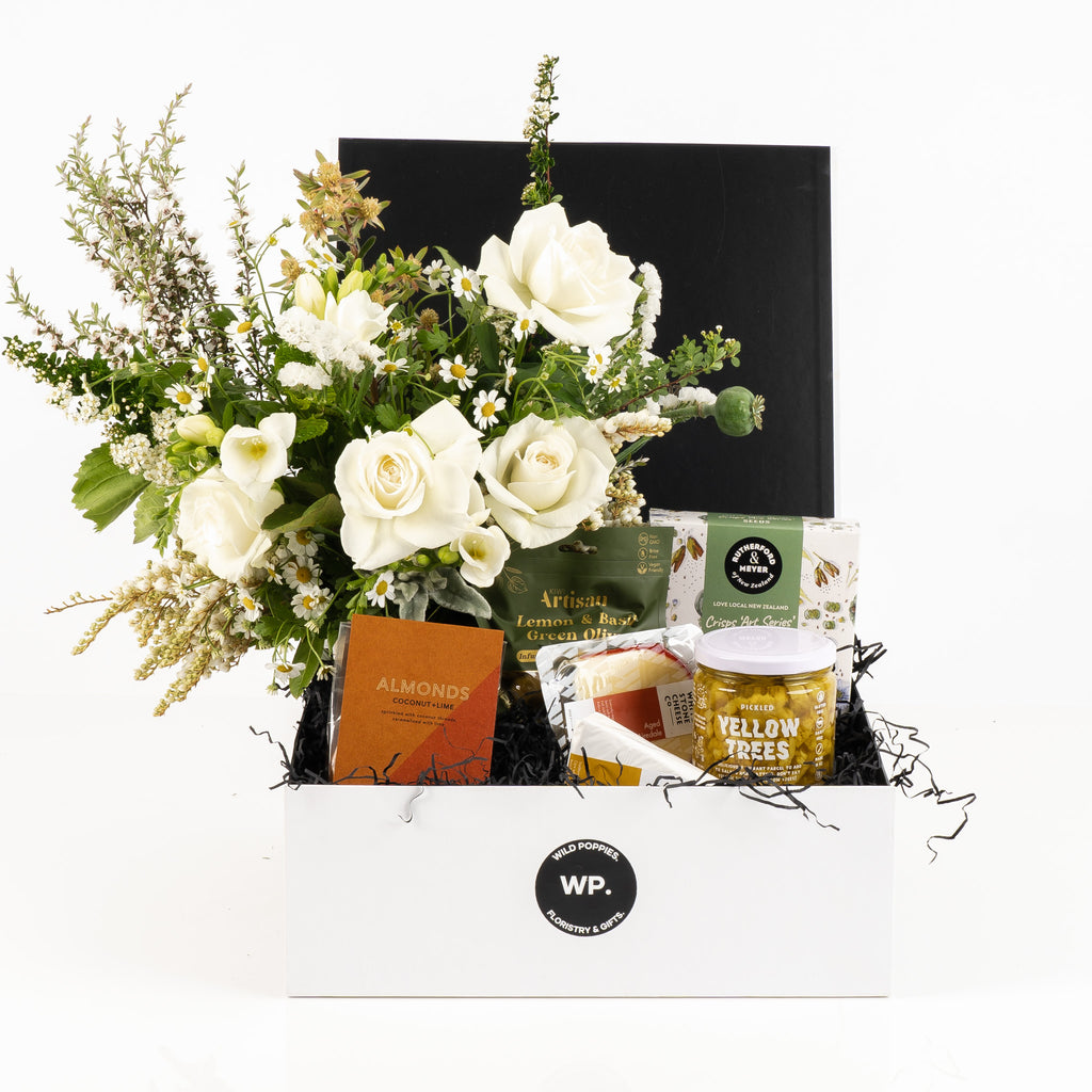 "A Home Staple Gift Hamper" featuring a fresh white and green posy, Kiwi Artisan lemon and basil green olives, Almonds Coconut and Lime, pickled yellow trees, White Stone Cheese Co. Aged Airedale and Brie, and Rutherford and Meyer crisps. All elegantly presented in a premium Wild Poppies gift box with tissue paper and satin ribbon, perfect for any occasion.