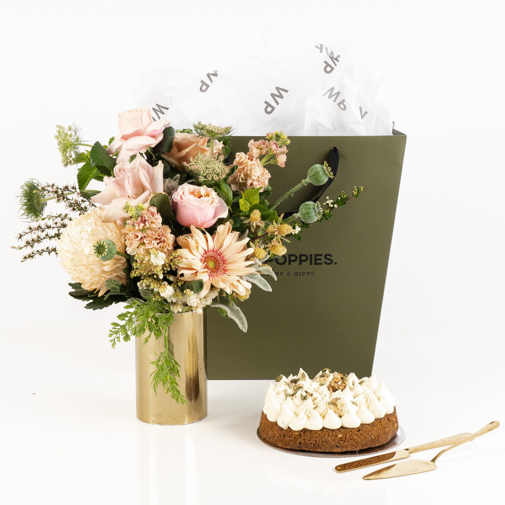 "Bouquet & Bake – Carrot Edition Gift" featuring a stunning fresh pastel bouquet paired with a moist, flavorful carrot cake. Presented in a premium Wild Poppies gift bag with satin ribbon and tissue paper, this elegant gift set is perfect for birthdays, celebrations, or any occasion, combining fresh florals with a delicious homemade treat.