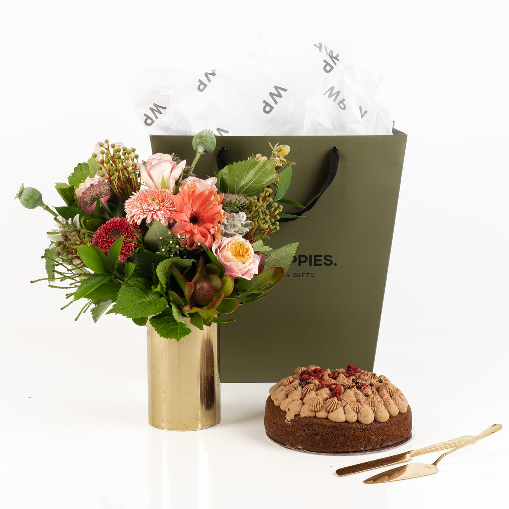 "Bouquet & Bake – Chocolate Edition Gift" featuring a vibrant pink and green bouquet paired with a decadent raspberry chocolate cake. Presented in a premium Wild Poppies gift bag with satin ribbon and tissue paper, this sweet and floral set makes a perfect gift for any occasion, offering a delightful combination of fresh florals and indulgent treats.